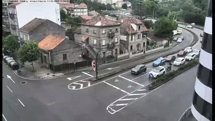 A wet street intersection with several cars and a few buildings visible, including a large grey house.