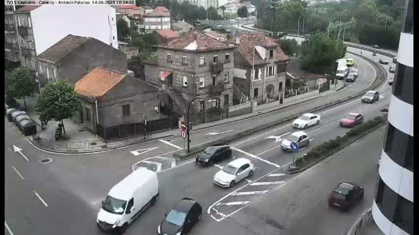 A street intersection in a town with several cars and buildings, under an overcast sky.