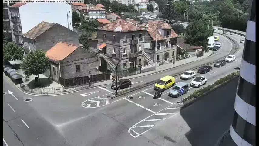 An aerial view of a street intersection in a residential area on a sunny day, with several cars parked and driving along a nearby road.