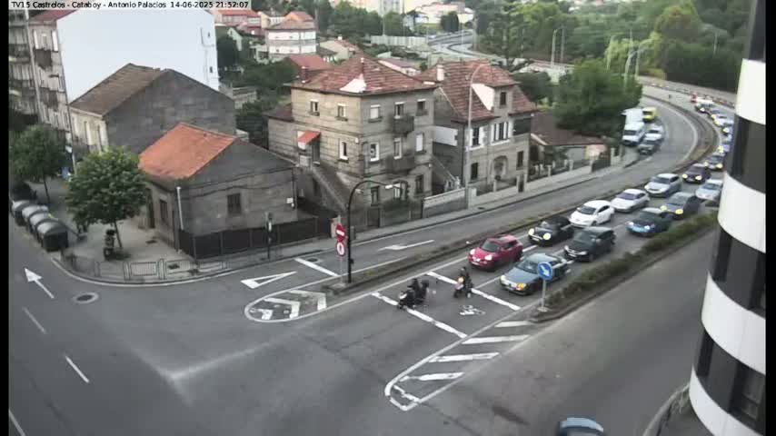 An aerial view of a street intersection in a residential area on a sunny day, with several cars parked and driving along a nearby road.