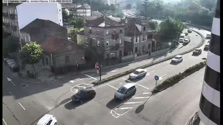 A street intersection with several cars, surrounded by buildings on a sunny day.