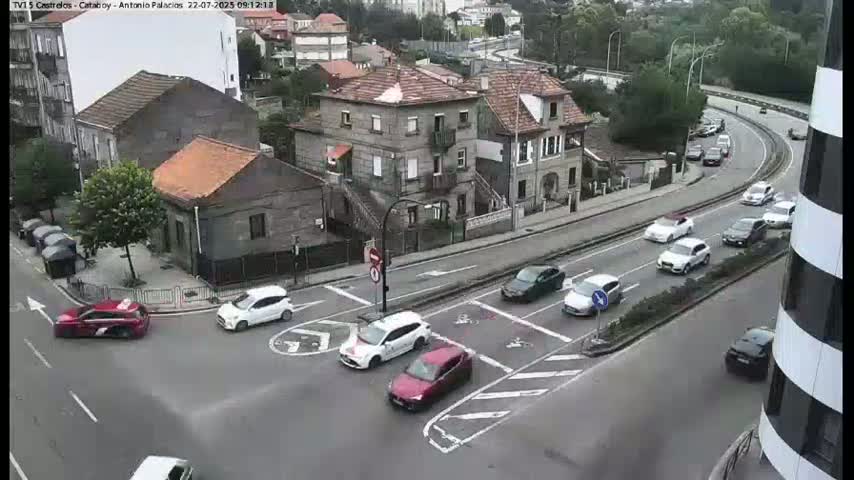 A street intersection with several cars, mostly white, and a few buildings, including a multi-story residential building, in an overcast setting.