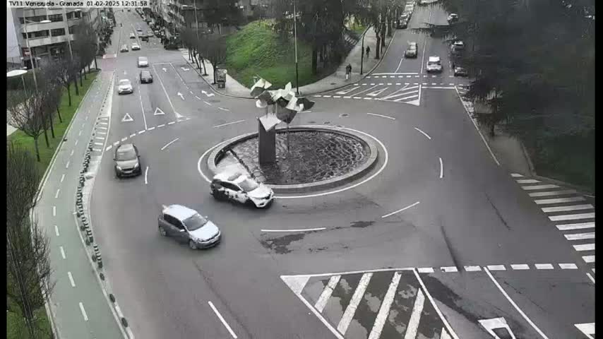 A traffic roundabout with several cars and a modern sculpture in the center, on an overcast day.