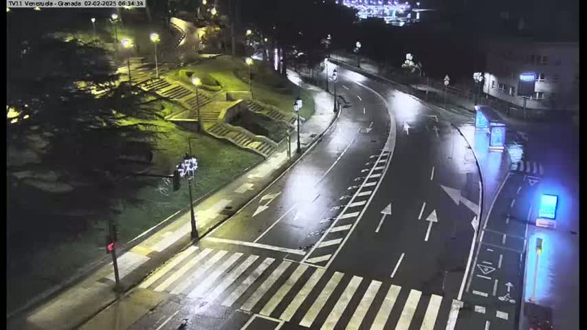 A wet, empty road curves through a nighttime park scene, with pedestrian crosswalks and stairs visible.