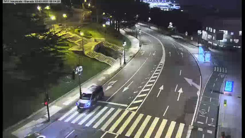 A silver SUV is crossing a pedestrian crosswalk on a curving, well-lit road at night.
