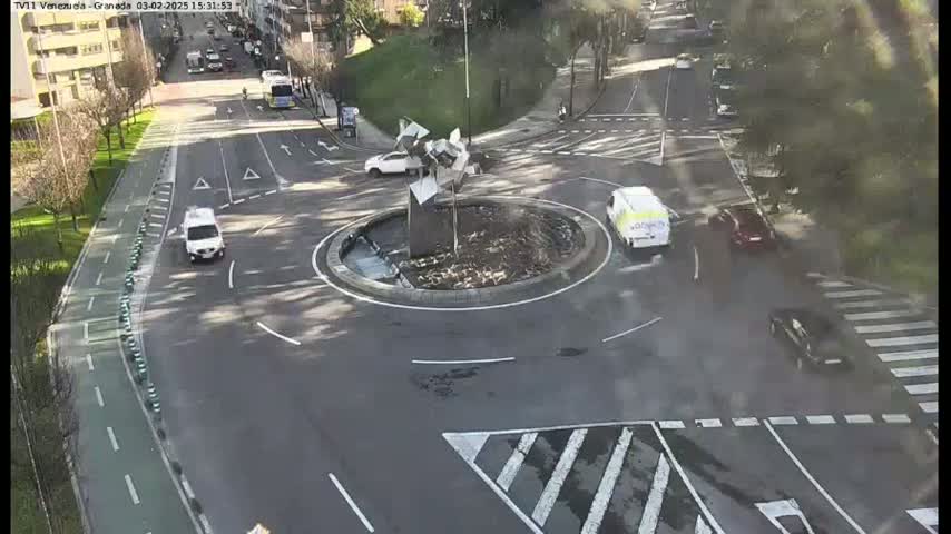 A roundabout with several cars and a modern sculpture in the center, under a mostly clear sky.