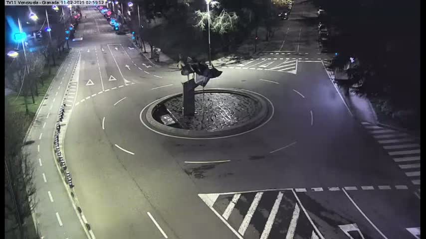 An overhead nighttime view shows a mostly empty roundabout with a dark sculpture in the center, surrounded by roads and pedestrian crossings.