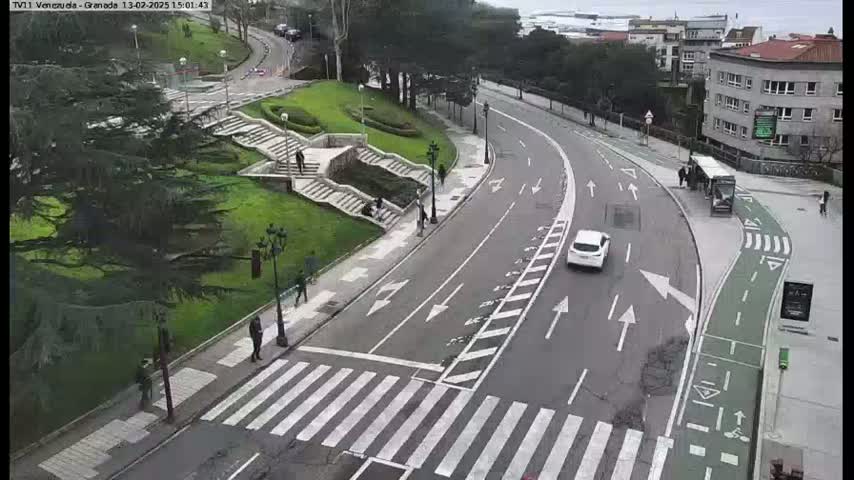 A curved road with a pedestrian crossing and bike lane runs through a park-like setting with stairs and greenery, under an overcast sky.