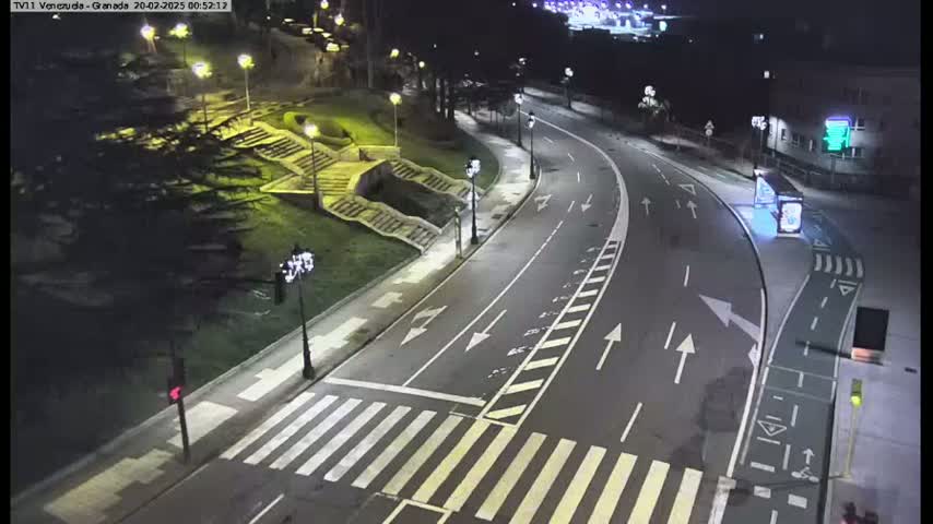 A nighttime, aerial view of a curving road with a crosswalk, streetlights, and stairs leading to a grassy area.