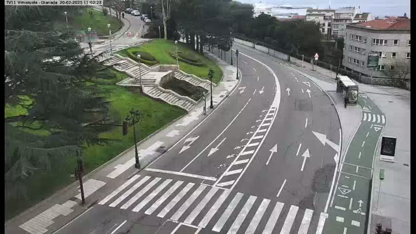 A curved road with crosswalks and a bike lane winds through a park-like area on an overcast day.