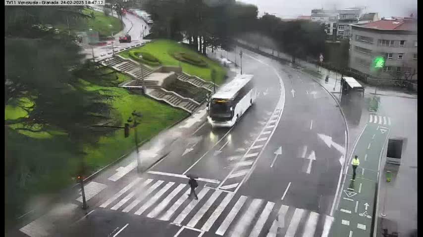 A wet, rainy street scene shows a white bus, a person crossing a crosswalk, and other pedestrians and vehicles on the road.