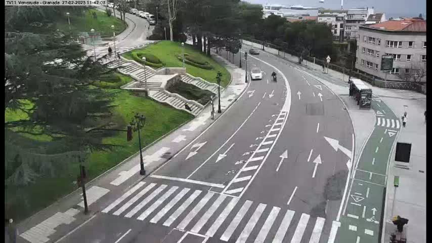 A curving road with a crosswalk and bike lane passes through a park-like area with stairs and greenery under an overcast sky.