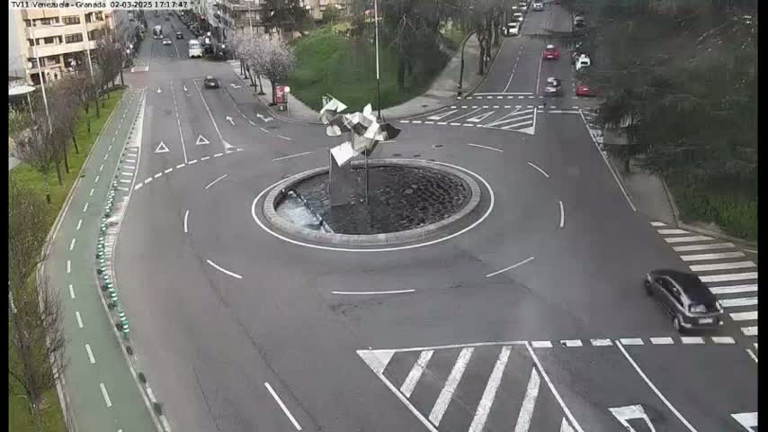 A roundabout with a modern metal sculpture in the center, surrounded by roads with light traffic, under a cloudy sky.