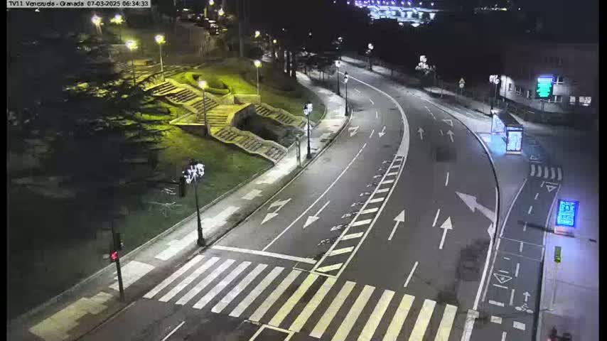 A nighttime aerial view shows a curved roadway with pedestrian crosswalks and stairs leading up to a landscaped area, lit by streetlights.