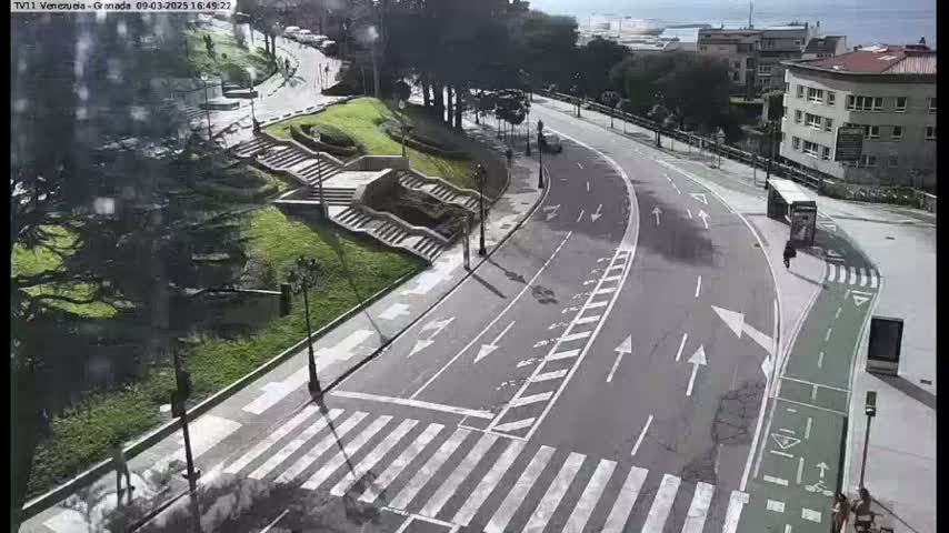 A curved road with a bike lane and pedestrian crossing winds through a city park on a partly sunny day.