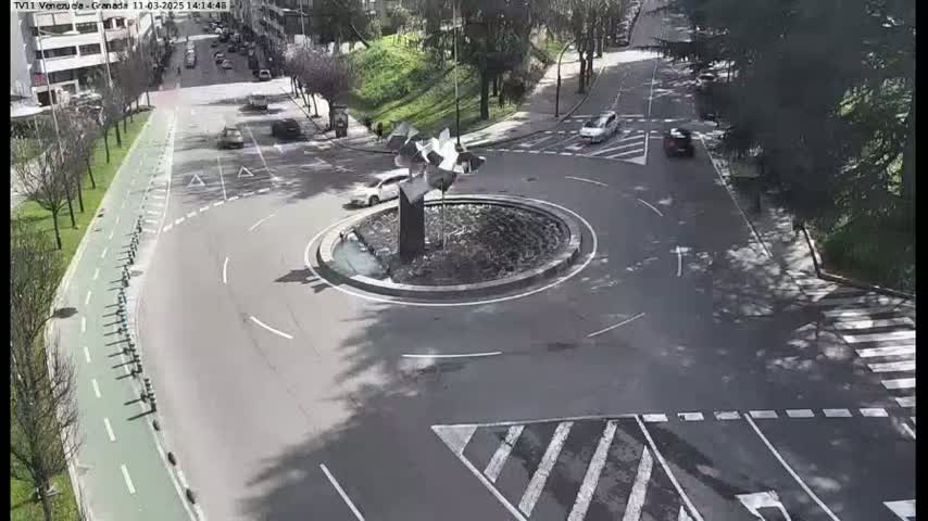 A roundabout with a modern sculpture in the center, surrounded by roads with several cars, on a sunny day.