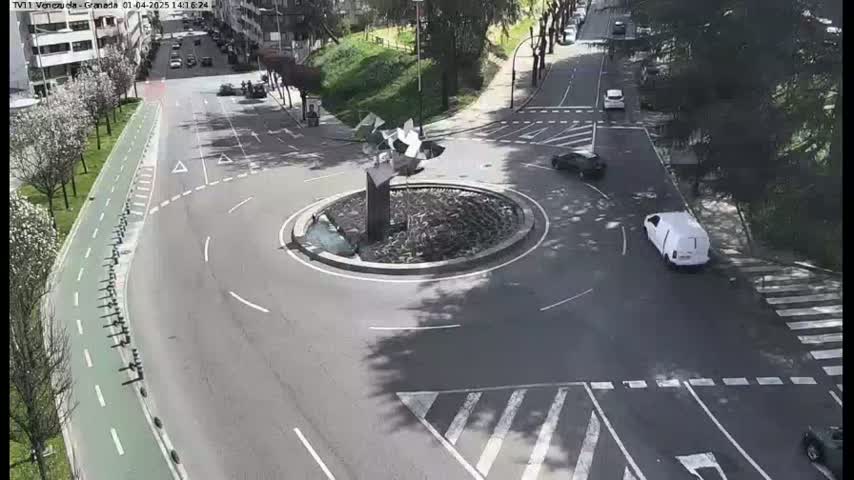 A roundabout with a few cars driving around it and a bike lane next to it, on a sunny day.
