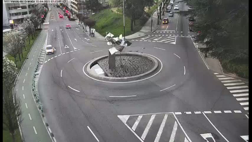 A roundabout with a modern sculpture in the center, surrounded by roads with several cars and a bike path, on an overcast day.