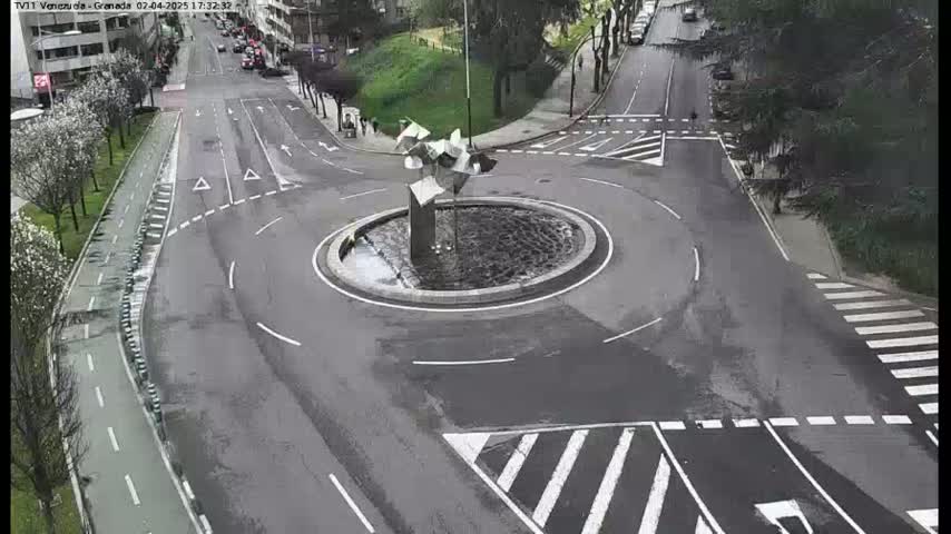 A roundabout with a modern sculpture in the center, surrounded by roads with pedestrian crossings and bike lanes, on a seemingly overcast day.