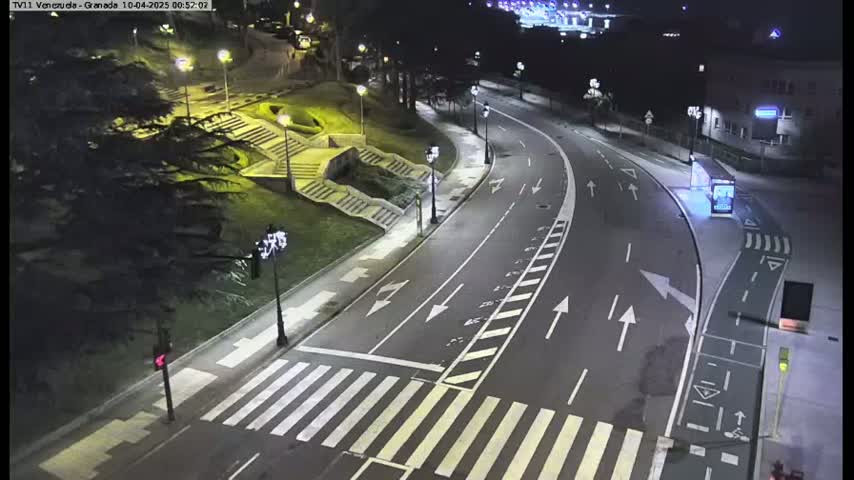 A nighttime, high-angle view shows a mostly empty roadway curving through a park-like setting with stairs and trees, illuminated by streetlights.