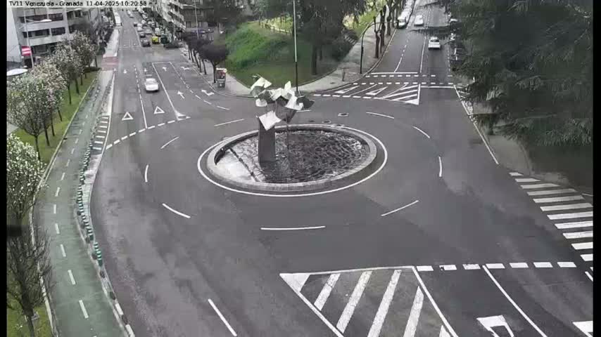 A wet roundabout with a modern sculpture in the center is surrounded by roads and a bike lane.