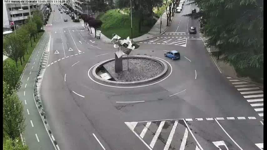 A roundabout with a modern metal sculpture in the center is surrounded by roads and a bike path, with a few cars visible on a mostly clear day.