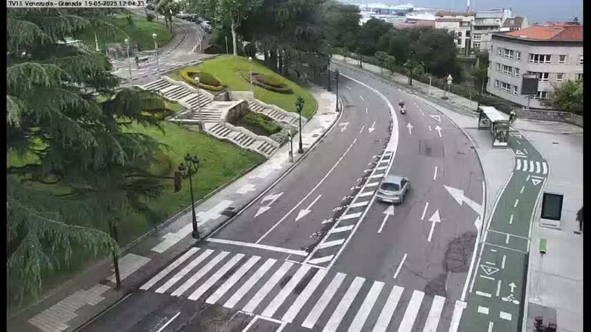 A curved road with a crosswalk and bike lane winds through a landscaped area with stairs and greenery, under overcast skies.