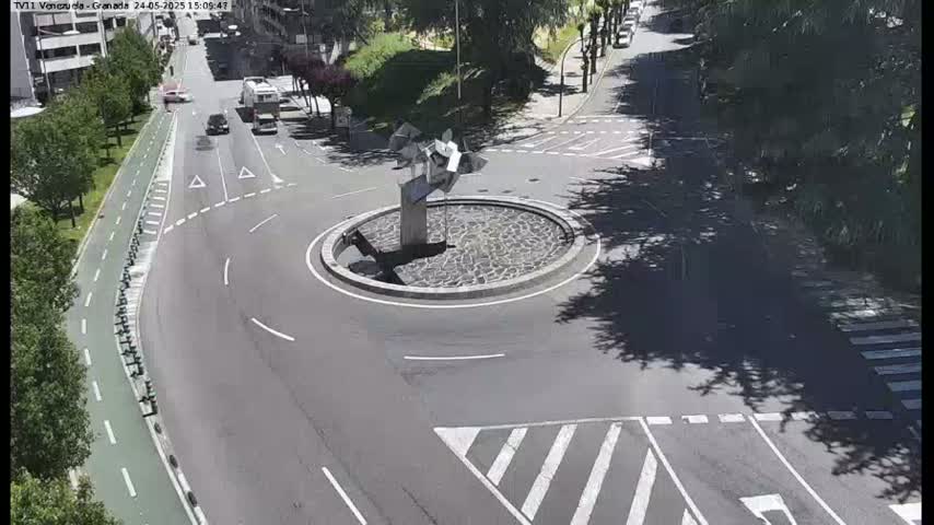 A roundabout with a modern sculpture in the center is surrounded by roads and a bike lane, on a sunny day.