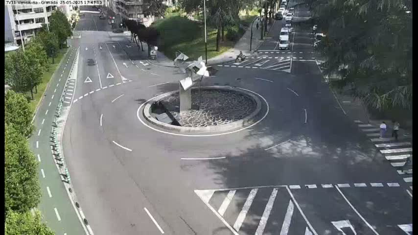 A roundabout with a modern sculpture in the center is surrounded by roads and pedestrian crossings on a sunny day.