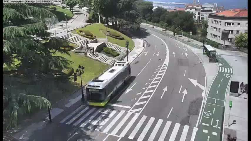 A bus is stopped at a crosswalk on a sunny day near a grassy area with stairs and trees.