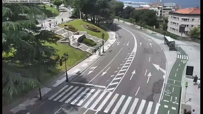 A curving roadway with crosswalks and bike lanes winds through a park-like area with stairs and greenery, under a partly sunny sky.