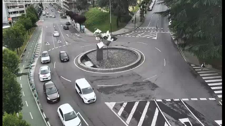 A roundabout with several cars driving around it and across intersecting roads, on an overcast day.