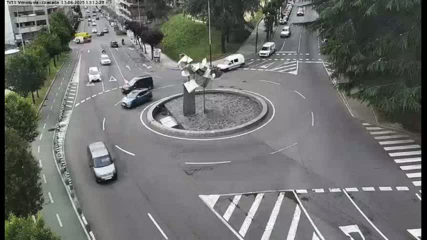 A roundabout with several cars driving around it, under an overcast sky.