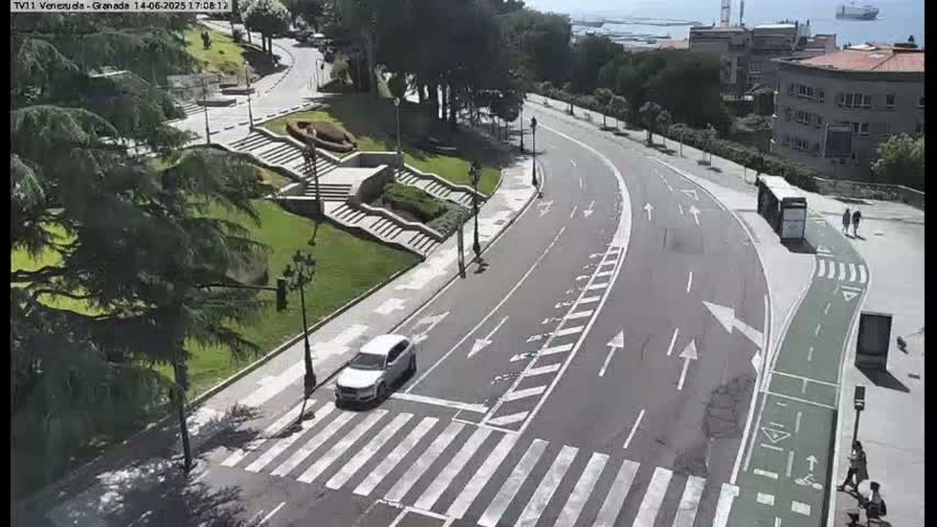 A sunny day shows a curving road with a pedestrian crossing and bike lane next to a park with stairs leading up a hillside.