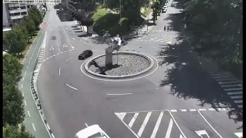A roundabout with a modern sculpture in the center, surrounded by roads with cars and pedestrian crossings, on a sunny day.