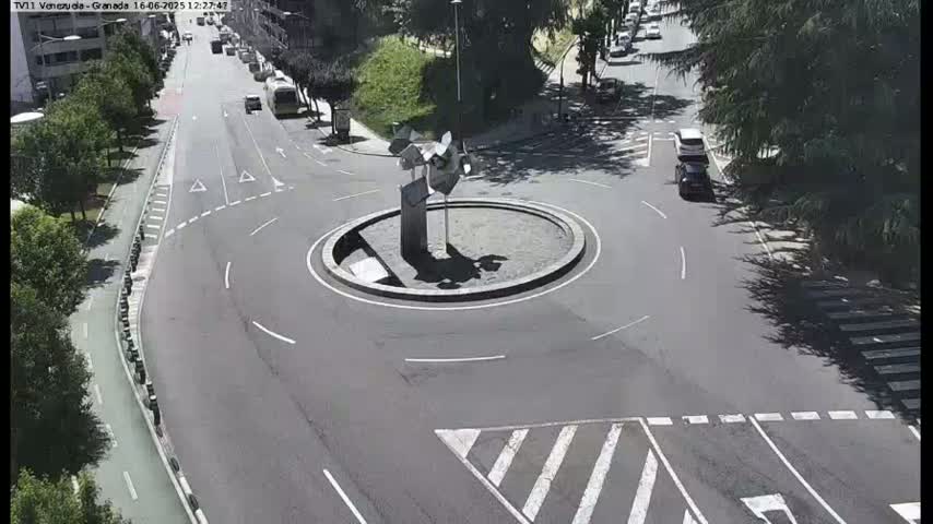 A circular roundabout with a modern sculpture in the center, surrounded by roads with a few cars, on a sunny day.