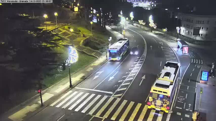 An elevated view captures a curved city street with a line of vehicles, including cars, a van, and a scooter at a crosswalk, a green bike lane, and pedestrians on sidewalks, all set against a backdrop of grassy hills with stone stairs and urban buildings under an overcast sky.