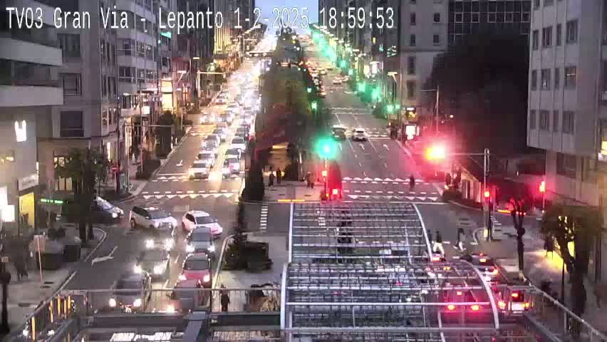 A busy city intersection at dusk, with cars moving in all directions, traffic lights, and buildings lining the street.