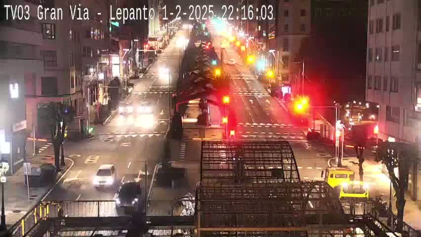 A nighttime view of a city street intersection with several cars and some trucks, under clear skies.