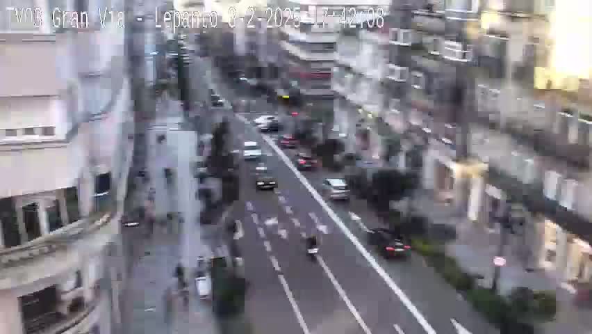 A high-angle view shows a city street with cars and pedestrians, under partly cloudy daytime conditions.