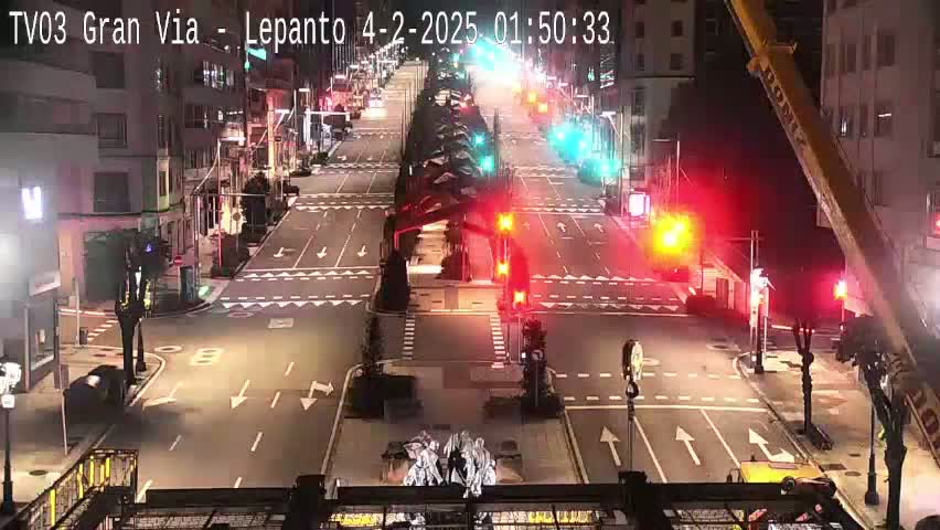 A nighttime, high-angle view of a mostly empty city street intersection with traffic lights and a construction crane.