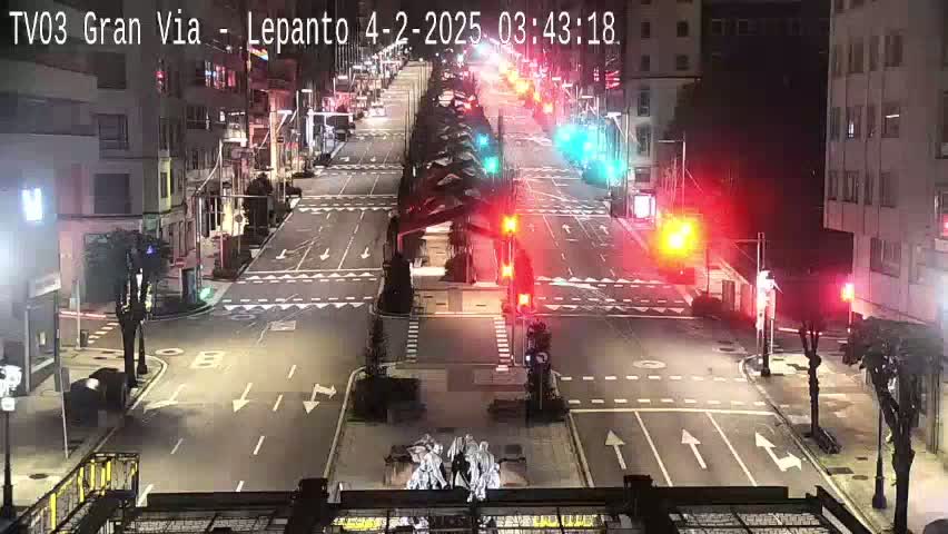 A nighttime, mostly empty city street intersection with traffic lights and some sparse streetlights, showing minimal vehicle traffic.