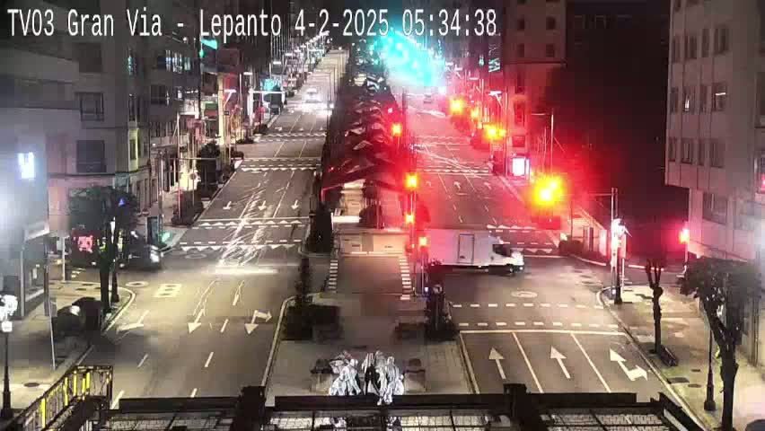 A nighttime view of a city street intersection with several cars and a van, illuminated by streetlights and traffic signals.