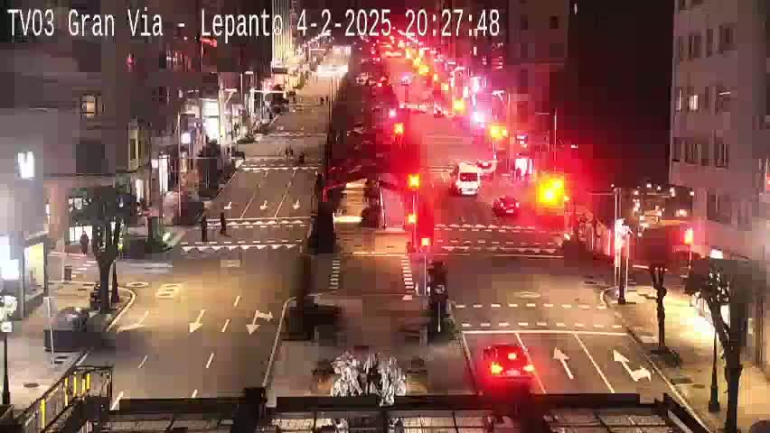A nighttime aerial view of a city intersection with several vehicles and streetlights, showing moderate traffic flow.