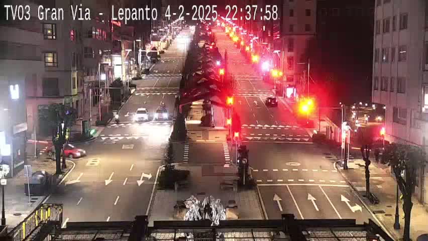 A nighttime, high-angle view of a city street intersection with several vehicles and traffic lights.
