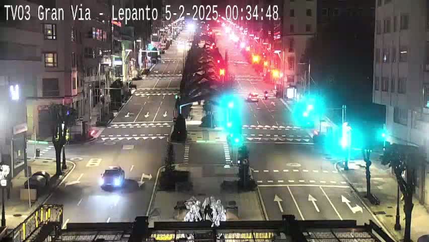 A nighttime, high-angle view of a city intersection with several cars and traffic lights, some of which are green.