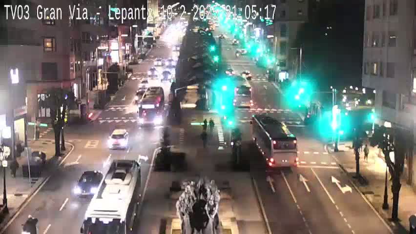 A nighttime, city street scene shows various vehicles, including cars and buses, navigating a multi-lane intersection under bright streetlights.