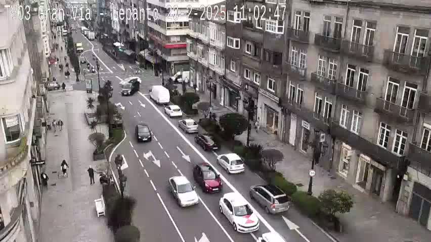 A street scene shows several cars driving down a city street lined with multi-story buildings on a cloudy day.