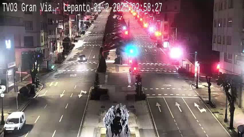 A nighttime, high-angle view of a city street intersection with sparse traffic and several vehicles at a standstill at traffic lights.
