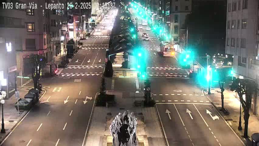 A nighttime, overhead view of a city intersection with several cars and a statue at its center, illuminated by streetlights.